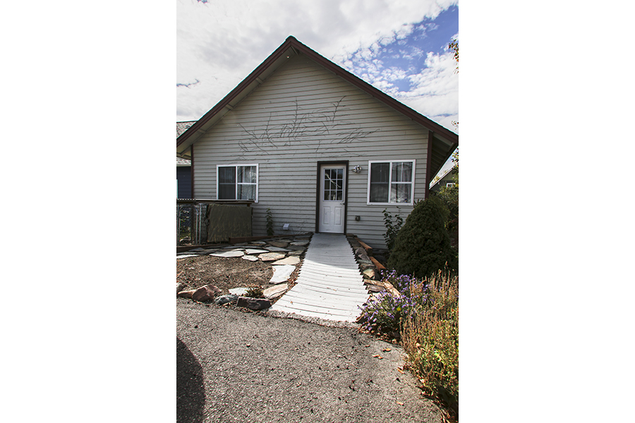 A close view of a wooden pathway leading to a white door. The path is bordered by paving stones.